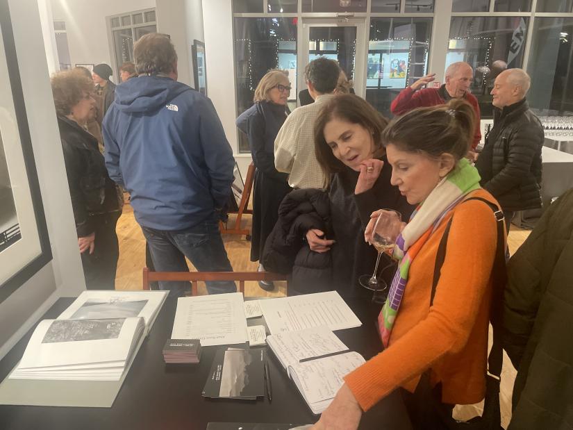 Kathy Plesser, at left in the foreground, and Amy Singer peruse books on Ruth Orkin’s work, sold at the gallery for Oblong Books. In the background, from left, Mary Engel, Lisa Aiba, Richard Block and Steve Aresty are deep in their respective conversations. Photo by Deborah Maier